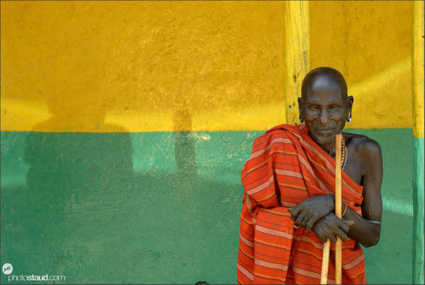 Old man and shadow - Samburu man in red blanket resting before colorful butchery wall, South Horr, Kenya